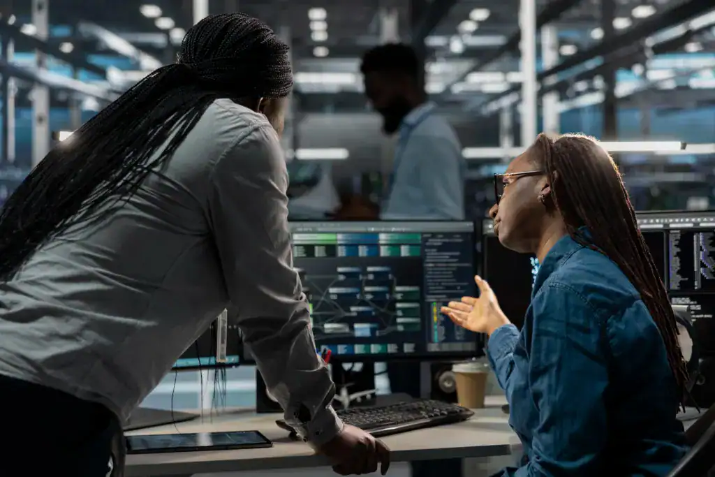 Two colleagues discussing a data workflow diagram on a monitor in a data centre office.
