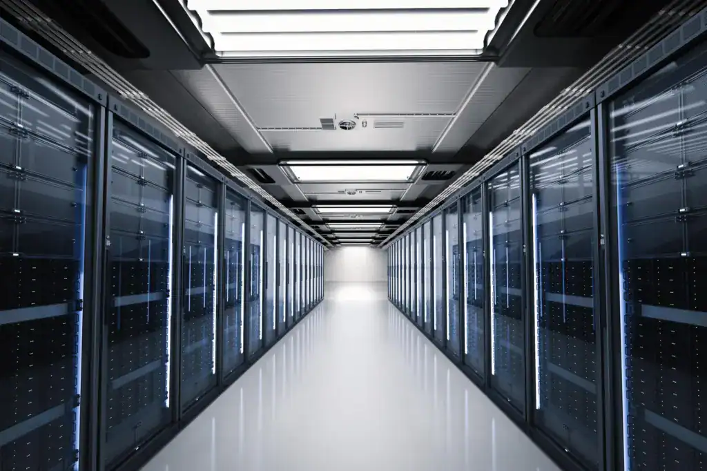 Long data centre aisle flanked by two rows of server racks lit in blue, leading to a bright doorway at the end