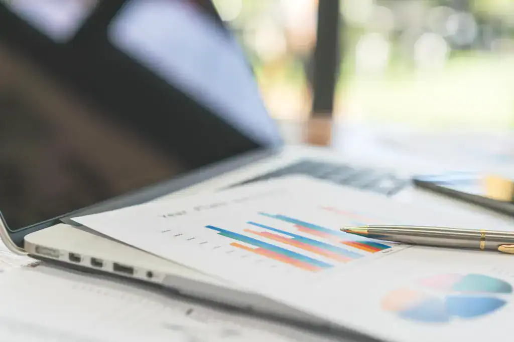 Laptop beside printed business reports with bar and pie charts