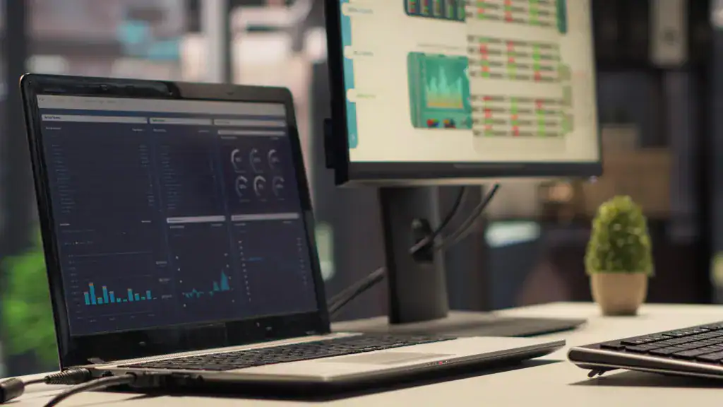 Office workstation with laptop and monitor displaying business analytics dashboards