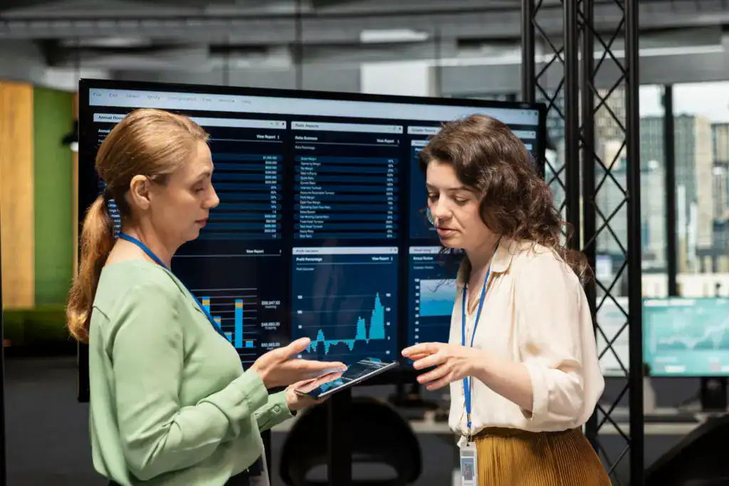 Two business professionals discussing financial data displayed on a dashboard